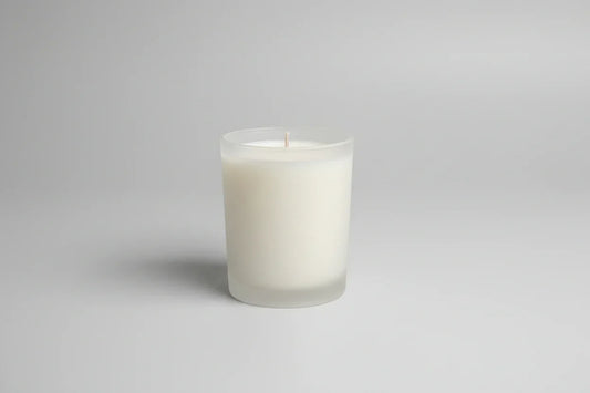 Handgemachte weiße Kerze im Glas, minimalistisch vor grauem Hintergrund, nachhaltige Deko