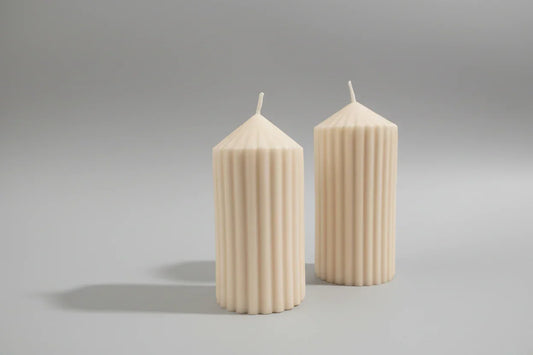 Zwei handgemachte, elfenbeinfarbene Stabkerzen mit geriffeltem Design auf grauem Hintergrund.
