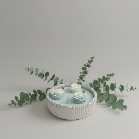 Handgemachte Kerze in blauer Schale mit Blumen-Dekor und Eukalyptus auf hellem Hintergrund