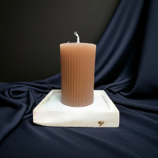 Handgemachte braune Kerze mit Rillen auf weißem Untersetzer, vor dunklem Stoffhintergrund