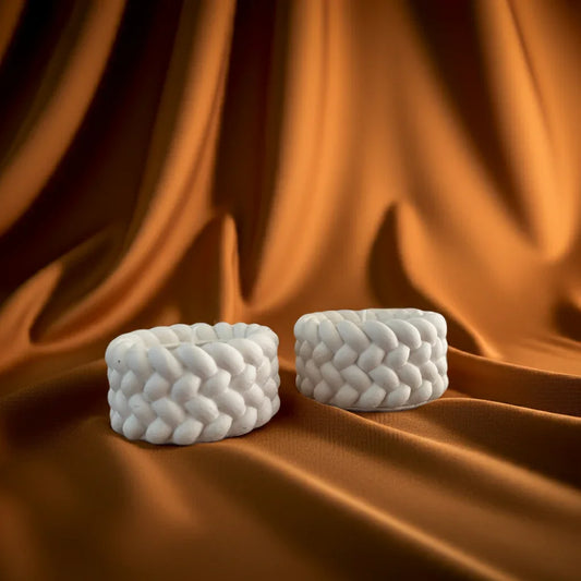 Zwei handgemachte, weiße Kerzen mit geflochtenem Muster auf braunem Stoff