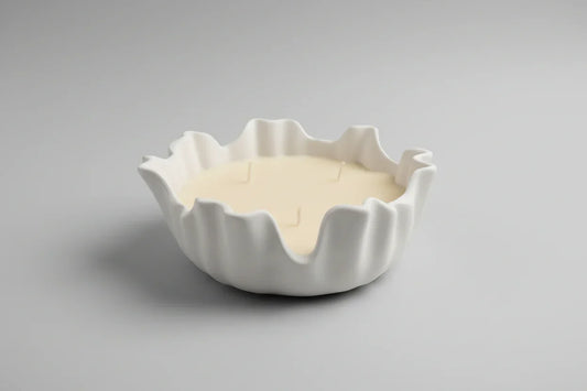 Handgemachte Kerze in weißer, wellenförmiger Schale auf neutralem Hintergrund