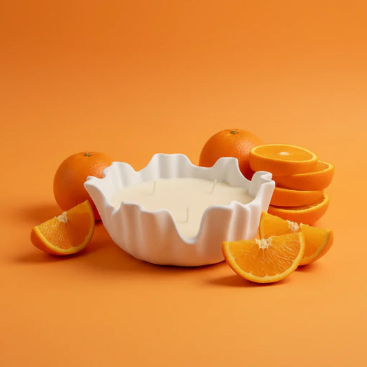 Handgemachte Kerze in weißer Schale mit frischen Orangenstücken, orangefarbener Hintergrund