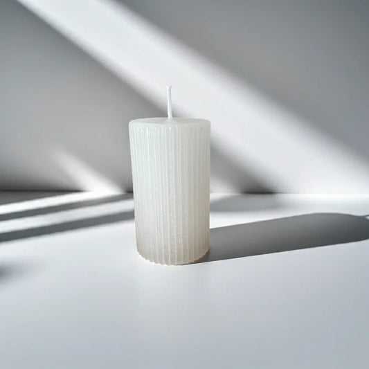 Weiße, handgemachte Kerze mit Rillenstruktur bei Tageslicht auf weißem Untergrund