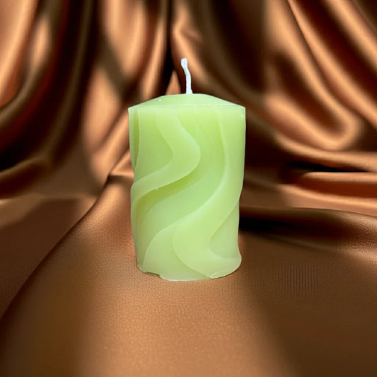 Handgemachte grüne Kerze mit Wellenmuster auf glänzendem, braunem Stoff