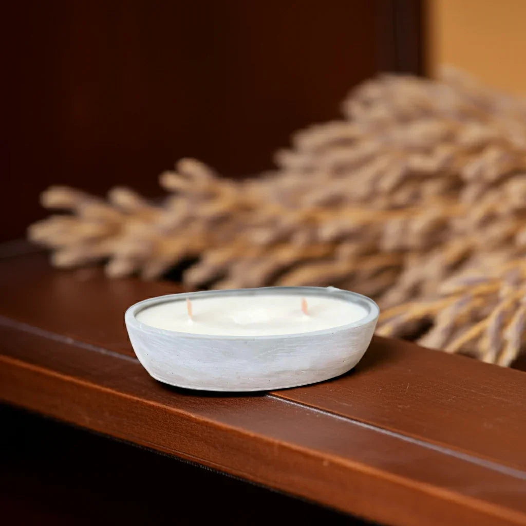 Handgemachte Kerze in weißer Schale, nachhaltige Deko vor getrocknetem Gras