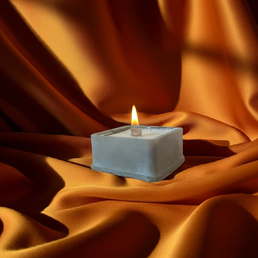 Brennende handgemachte Kerze im Betonwürfel mit Holzdocht auf orangefarbenem Stoff