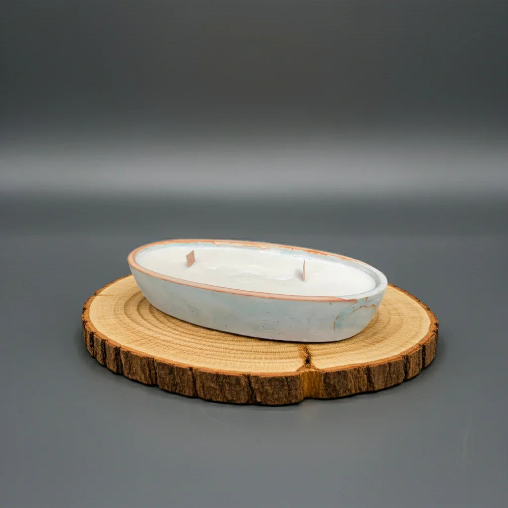 Ovale handgemachte Kerze mit Holzdochten in Keramikschale auf Holzscheibe, Deko