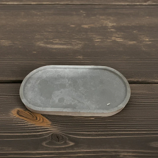 Graues Tablett aus Beton im Oval auf dunkler Holzoberfläche, minimalistisch dekorativ