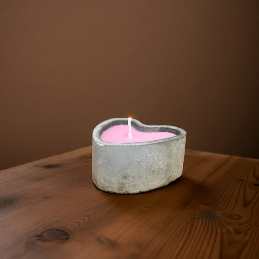 Handgemachte pinke Kerze in Herzform aus Beton auf Holztisch, stimmungsvolles Licht