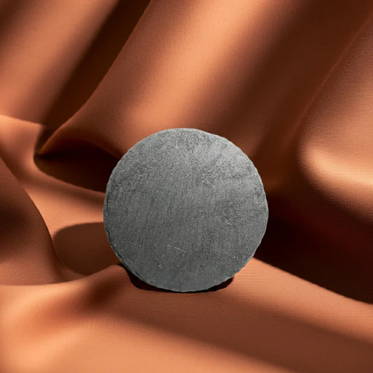 Runde Schieferplatte als Kerzenuntersetzer auf braunem Stoff drapiert