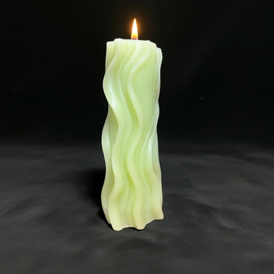 Handgemachte Wellen-Kerze in sanftem Grün, brennend vor schwarzem Hintergrund