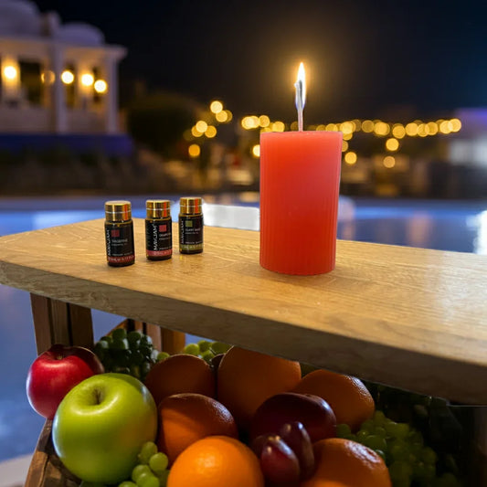 Rote Kerze brennt auf Holztisch neben Duftöl, frisches Obst im Vordergrund, stimmungsvolle Abendbeleuchtung