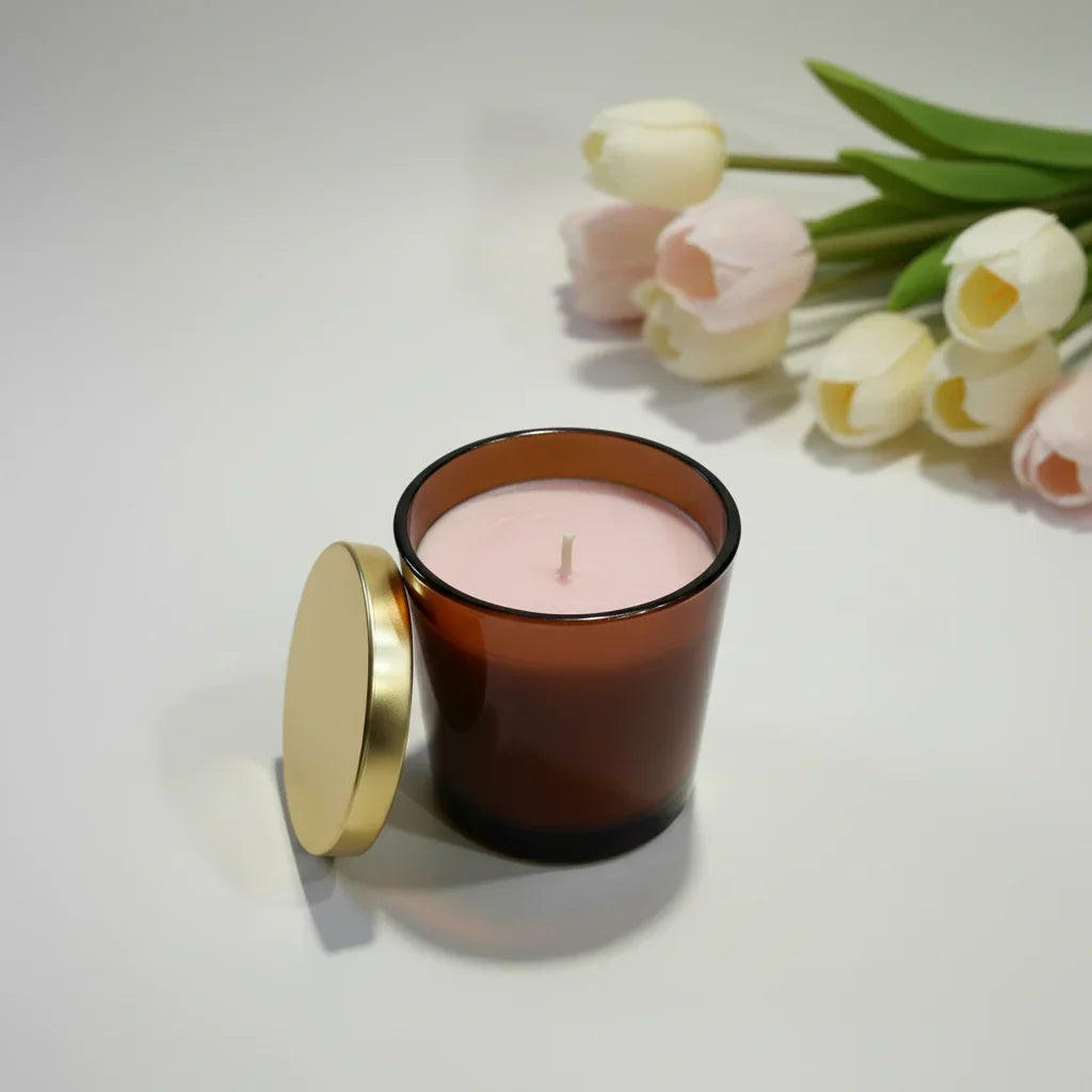 Handgemachte Duftkerze im braunen Glas mit goldenem Deckel, daneben Tulpen