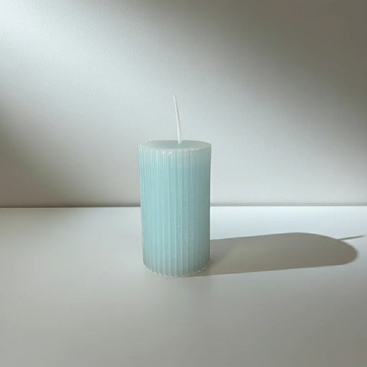 Handgemachte, hellblaue Stumpenkerze mit geriffelter Oberfläche auf weißem Hintergrund