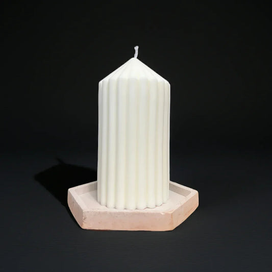 Weiße, handgemachte Stumpenkerze mit Rillenmuster auf sechseckiger Unterlage, schwarzer Hintergrund