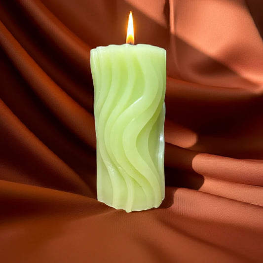 Handgemachte grüne Kerze mit Reliefmuster brennt auf braunem Stoff, stimmungsvolles Licht