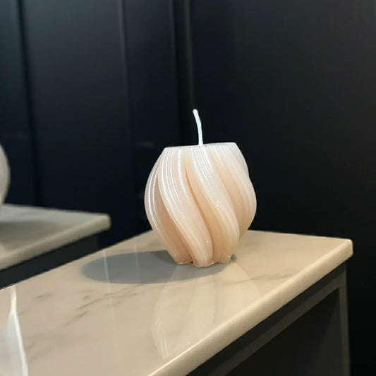 Handgemachte Kerze in moderner, gedrehter Form auf Marmoroberfläche vor dunklem Hintergrund