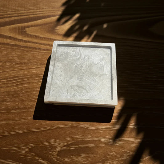 Quadratische Betonschale als Kerzenuntersetzer auf Holztisch mit Sonnenlicht und Schatten