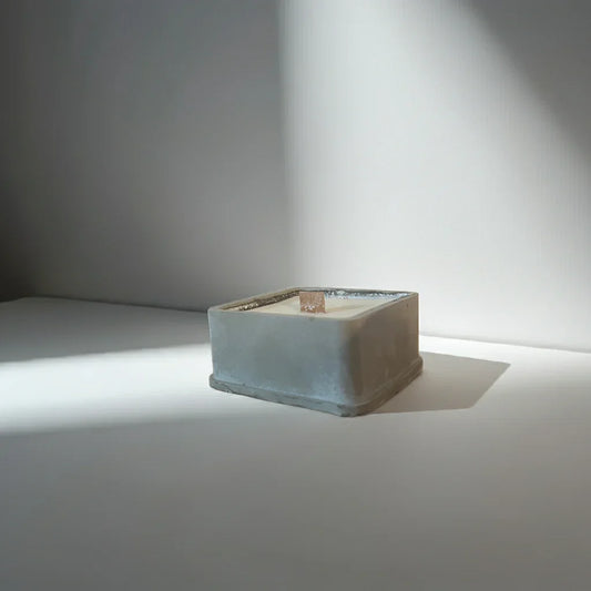 Quadratische handgemachte Kerze im Betonbehälter mit Holzdocht im Licht, minimalistisch