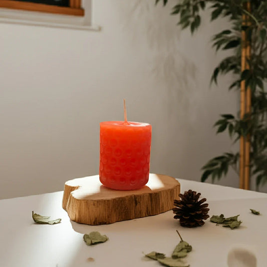 Handgemachte rote Kerze mit Relief auf Holzbrett, dekoriert mit Tannenzapfen und Blättern