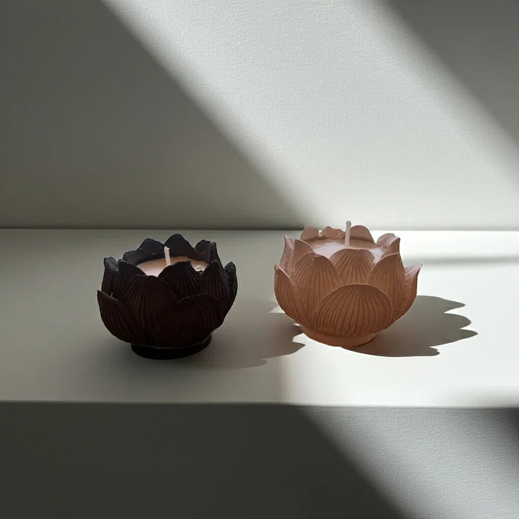 Zwei handgemachte Kerzen in Lotusblütenform, nachhaltig, auf weißer Oberfläche im Sonnenlicht.