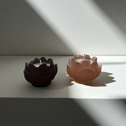 Zwei handgemachte Kerzen in Lotusblütenform, nachhaltig, auf weißer Oberfläche im Sonnenlicht.