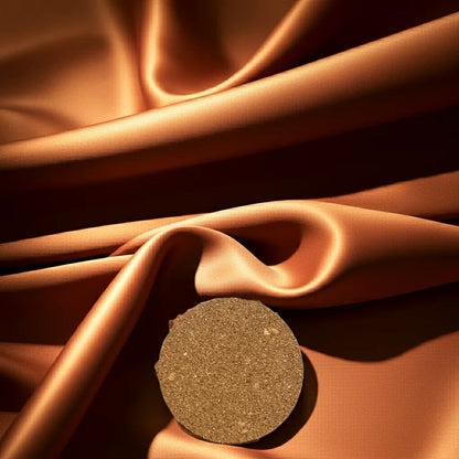 Handgemachte Kerze rund auf goldener, glänzender Stoffoberfläche, nachhaltiges Design