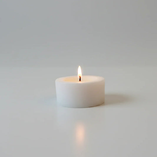 Weiße handgemachte Kerze brennt auf hellem Untergrund, stimmungsvolles Licht