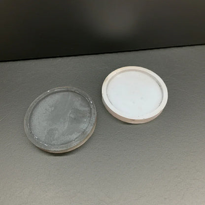 Zwei runde Kerzenuntersetzer aus Beton in Weiß und Grau, auf dunklem Hintergrund