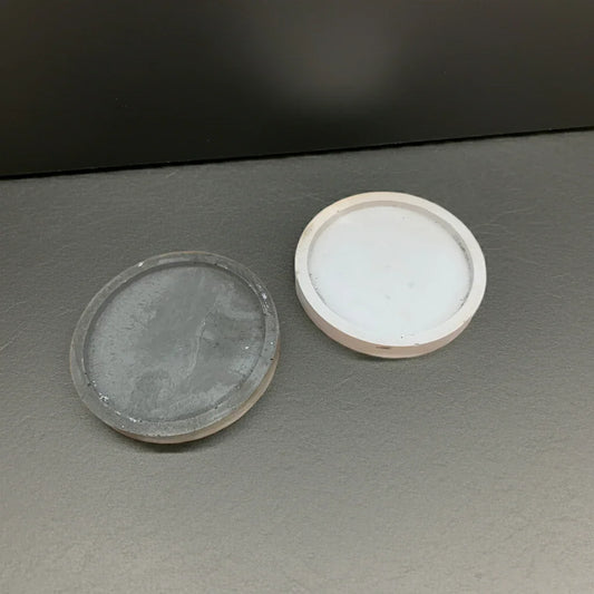 Zwei runde Kerzenuntersetzer aus Beton in Weiß und Grau, auf dunklem Hintergrund