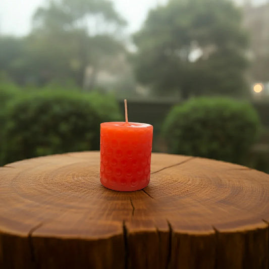 Rote handgemachte Kerze mit Muster auf Baumstamm, Natur im Hintergrund, stimmungsvolles Licht