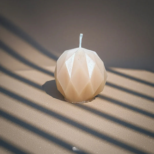 Handgemachte Kerze in geometrischer Form, beige, auf sandigem Hintergrund im Sonnenlicht