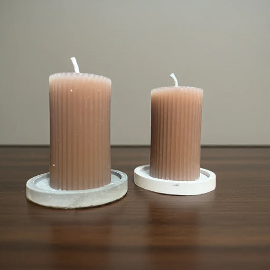 Zwei handgemachte, gerippte Kerzen in Naturfarben auf weißen Untersetzern, Holzoberfläche
