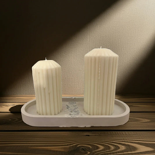 Zwei handgemachte weiße Stumpenkerzen mit Rillenmuster auf Tablett, Holzuntergrund.
