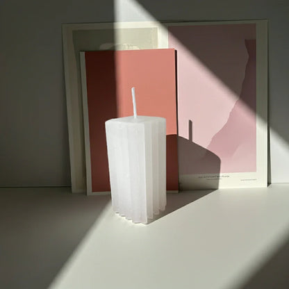 Weiße, handgemachte Kerze im modernen Design vor minimalistischem Hintergrund mit Sonnenlicht.