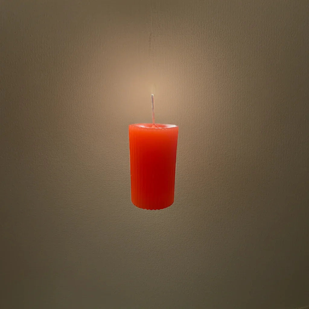 Handgemachte, orange Kerze leuchtet vor neutralem Hintergrund