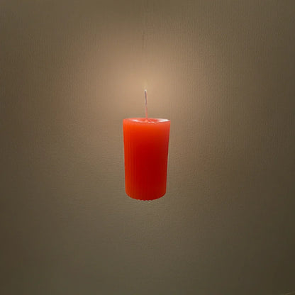 Handgemachte, orange Kerze leuchtet vor neutralem Hintergrund