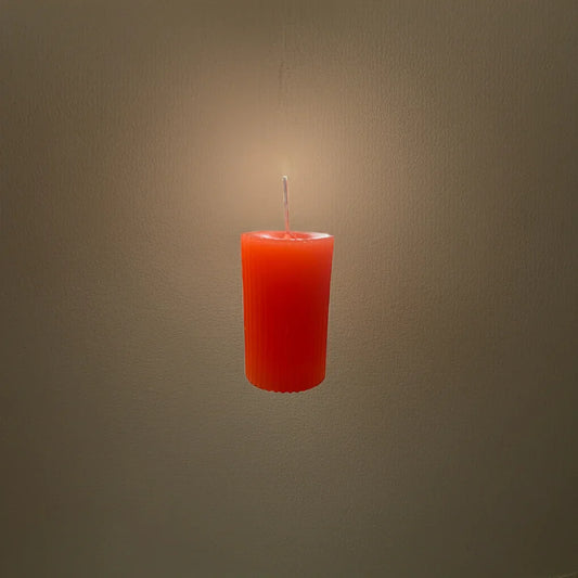 Handgemachte, orange Kerze leuchtet vor neutralem Hintergrund