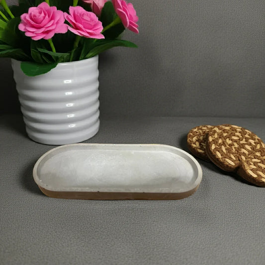 Handgemachte ovale Kerzenschale aus Beton, daneben Untersetzer und Blumentopf mit rosa Blumen