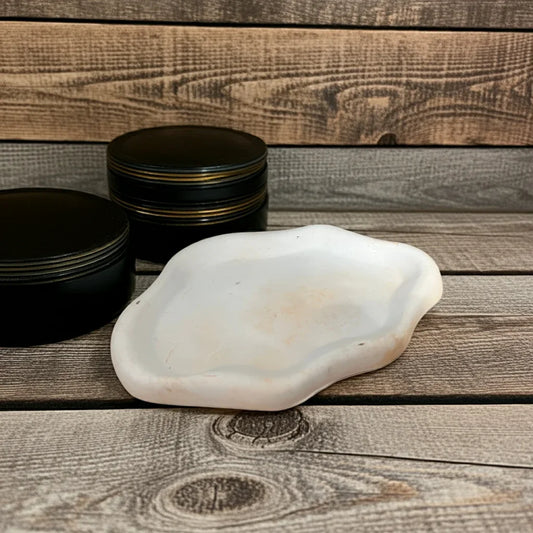 Handgemachtes weißes Kerzentablett aus Keramik vor zwei schwarzen Dosen auf Holzuntergrund