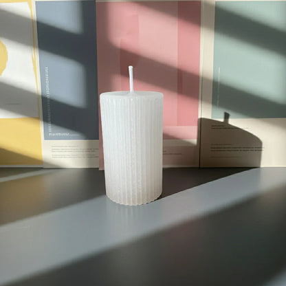 Weiße, handgemachte Kerze mit Rillenstruktur auf einem Tisch im Sonnenlicht, minimalistisch