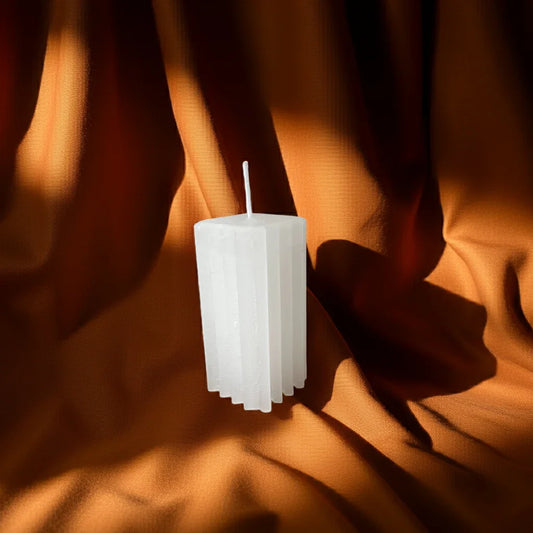 Handgemachte weiße Kerze mit geometrischem Design vor braunem Stoffhintergrund