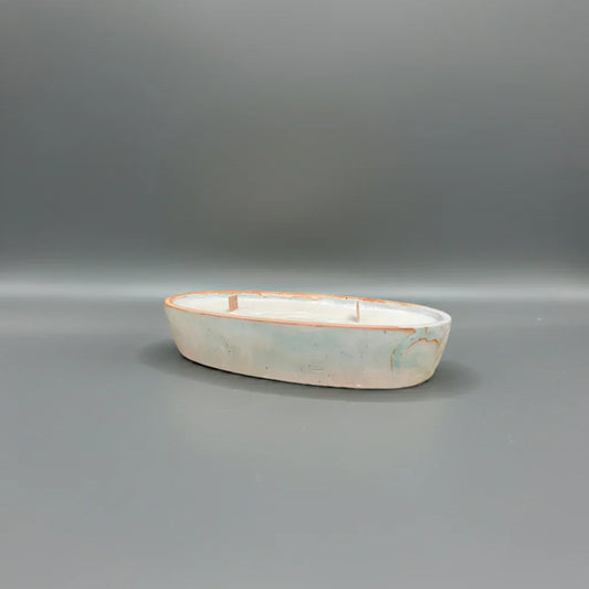 Handgemachte Kerze in ovaler Keramikschale mit drei Dochten auf grauem Hintergrund