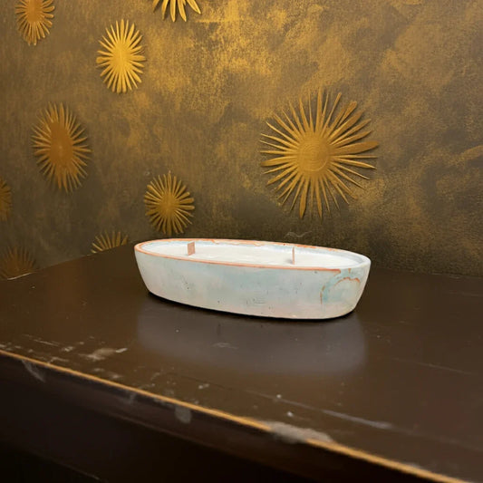 Handgemachte Kerze in ovaler Schale vor goldener Wand mit Sonnenmotiv-Deko