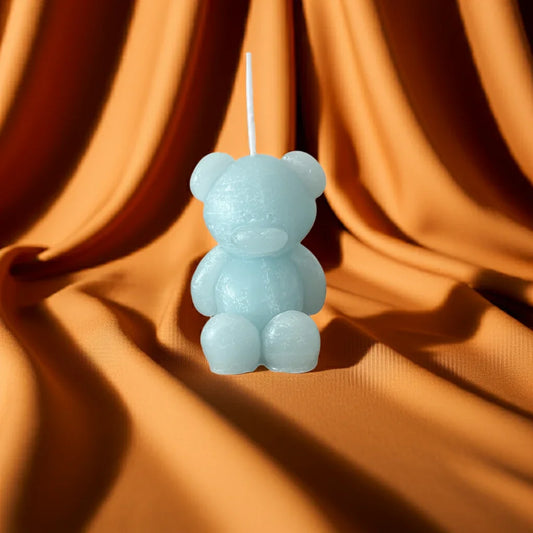 Handgemachte Kerze in Bärenform, hellblau, vor orangefarbenem Stoff drapiert