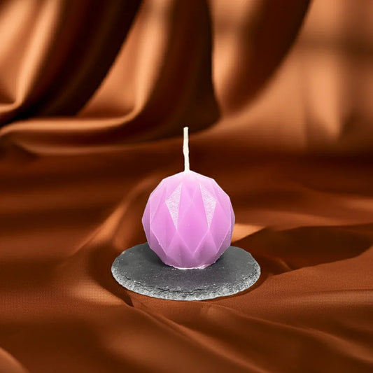 Handgemachte lila Kerze in Kugelform mit Facetten auf schwarzem Untersetzer vor braunem Stoff